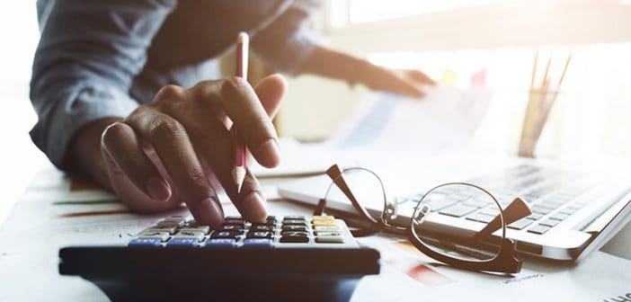 Close up of businessman or accountant hand holding pen working on calculator to calculate business data, accountancy document and laptop computer at office, business concept