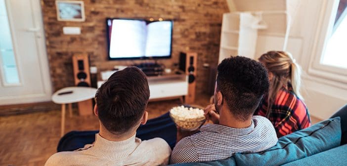 Friends watching tv and eating popcorn, rear view.