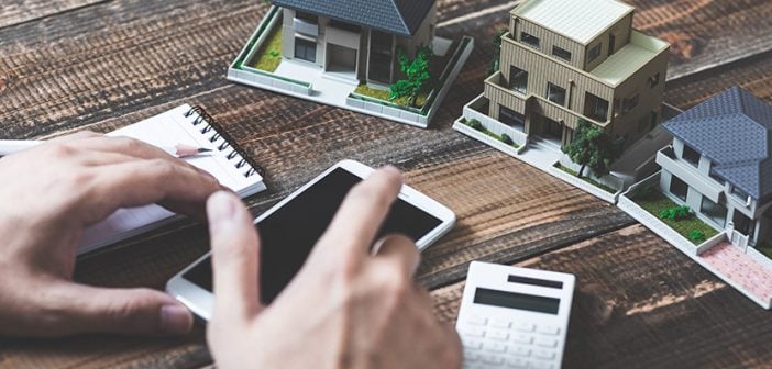 real estate investment small plastic property models on wooden surface with notepad, calculator, smartphone, male hands in view