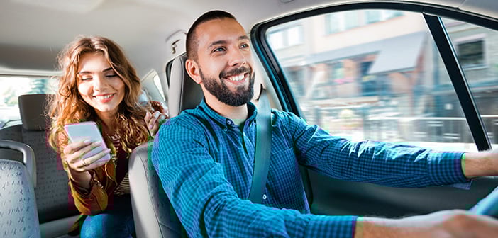 male ride share driving in front seat of car female passenger in back with cell phone in hand