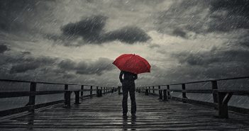 6 Ways to Prepare for the Next Market Crash A woman holds a red umbrella on a fishing pier during a storm.