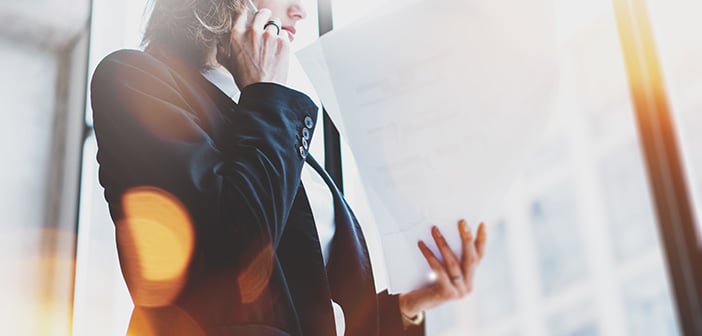 business woman wearing white shirt, talking smartphone and holding documents in hands. Open space loft office.