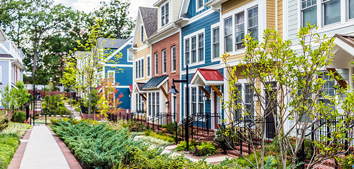 Row of colorful, red, yellow, blue, white, green painted residential townhouses, homes, houses with brick patio gardens in summer