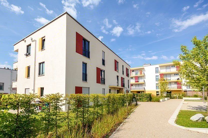 white apartment building with colorful window trim blue sky in background manicured grass and walkway
