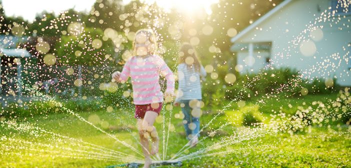 Adorable little girls playing with a sprinkler in a backyard on sunny summer day. Cute children having fun with water outdoors. Funny summer games for kids.