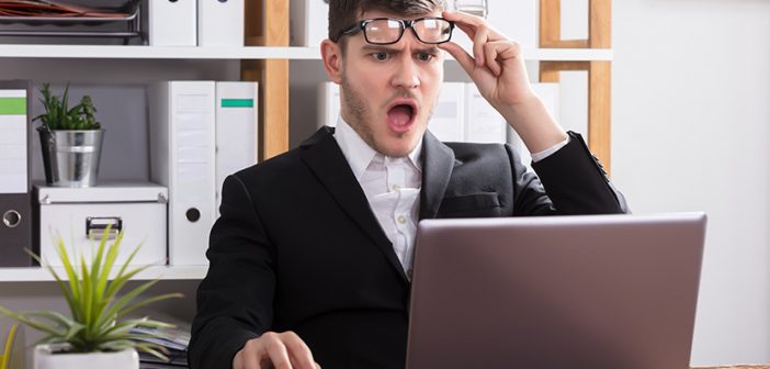 Shocked Young Businessman Looking At Laptop In Office