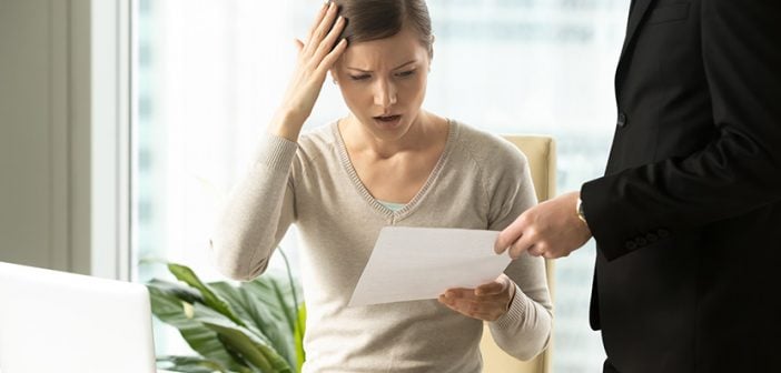 Puzzled businesswoman being presented lawsuit paperwork at desk in office 