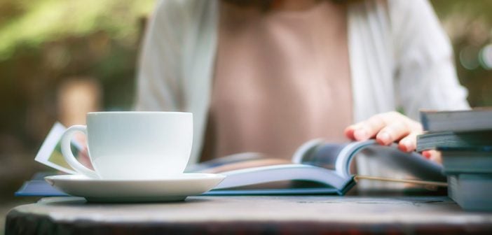 Close up of woman reading a book and drinking coffee in the garden.