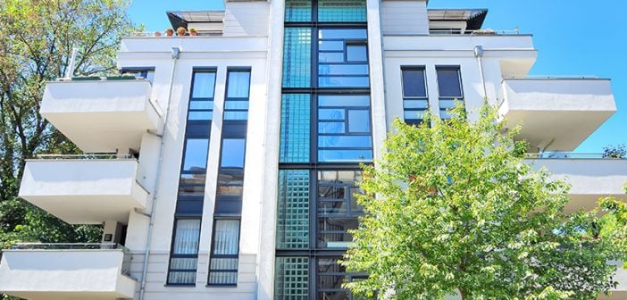 medium size apartment building with light gray cement exterior and lots of windows against a vibrant blue sky
