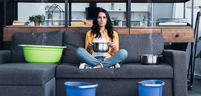 Beautiful woman with pots and buckets dealing with water damage in living room