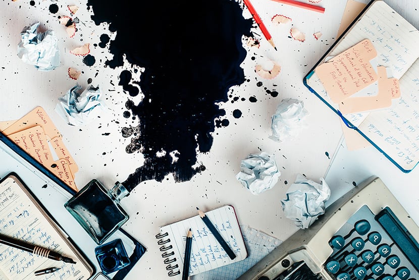 Writer workplace with spilled ink, stationery and a typewriter. Crumpled paper balls with pencils on a white wooden background, creative writing concept.