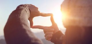 Close up of woman hands making frame gesture with sunrise on mou