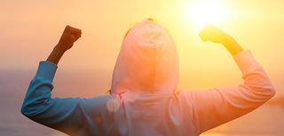 Back view of strong motivated woman celebrating workout goals towards the sun. Morning healthy training success.