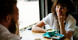 two people sitting in a cafe at a table drinking coffee smiling