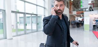 man on cell phone in airport wheeling suitcase